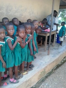 School children in Ghana apprehensively await their turn to take medicine that will help them stay healthy. Photo: FHI360