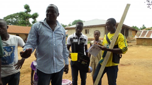 The Kenema District NTD Focal Point taking his NTD treatment in front of community members in Komende Luyama, Sierra Leone. Photo: FHI360